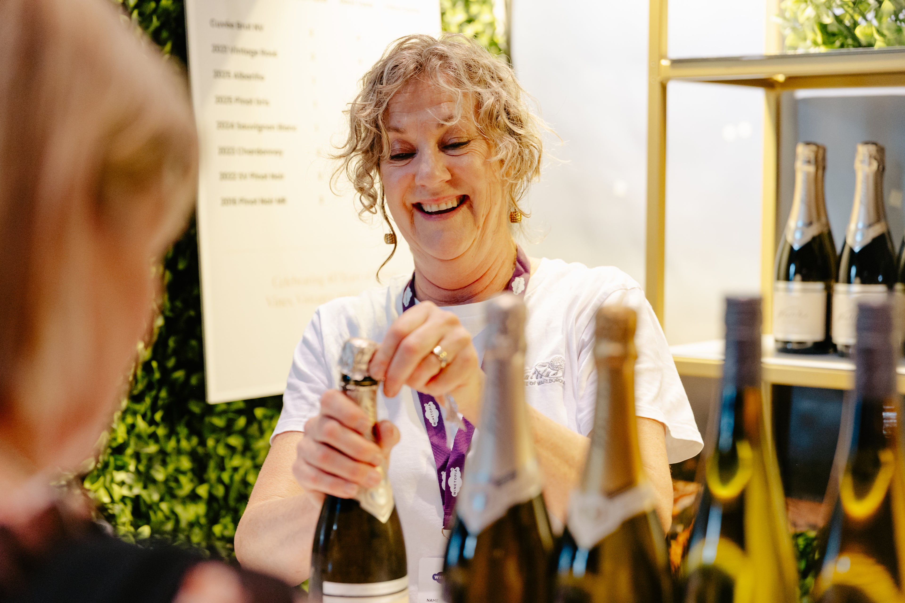 Woman opening a bottle of champagne with a blurred person in the foreground